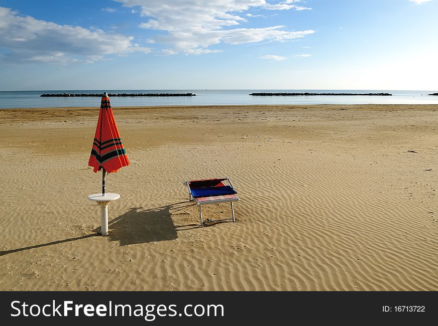 Orange umbrella and sunbed on a deserted beach in early morning