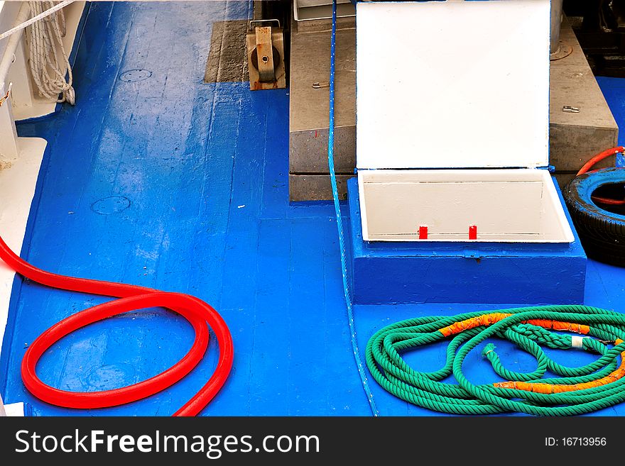 Blue deck of a fishing boat moored in the harbor with ropes and red hose