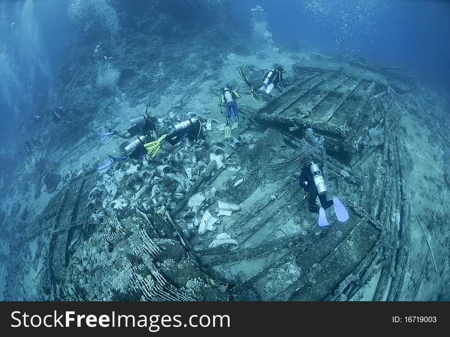 Group of scuba divers exploring the wrecked remains of a ship and its cargo. Yolanda reef, Ras Mohamed National Park, Red Sea, Egypt. Group of scuba divers exploring the wrecked remains of a ship and its cargo. Yolanda reef, Ras Mohamed National Park, Red Sea, Egypt.