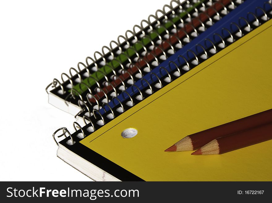 Blue, red, yellow and green school notebooks with red pencils on white background. Soft focus on pencil points. Copy space. Blue, red, yellow and green school notebooks with red pencils on white background. Soft focus on pencil points. Copy space.