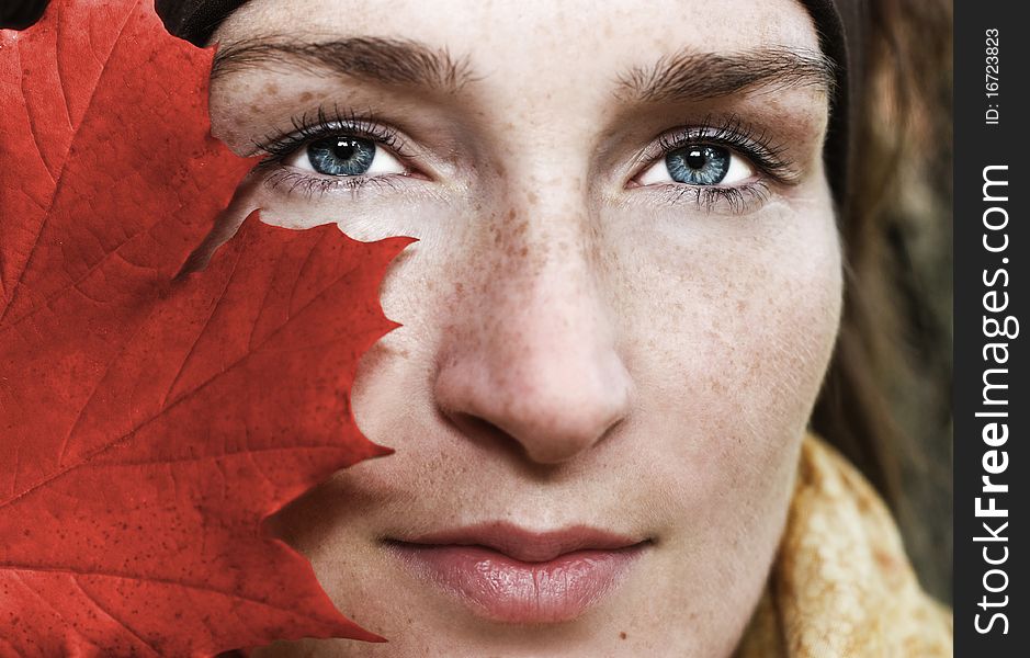 Woman face-half hidden behind the red leaf. Woman face-half hidden behind the red leaf