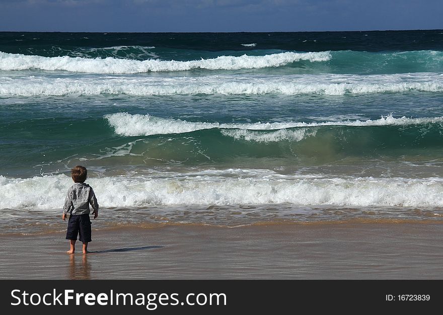 3-year-old boy looks at the sea. Autumn sea, strong waves, sharp colors.