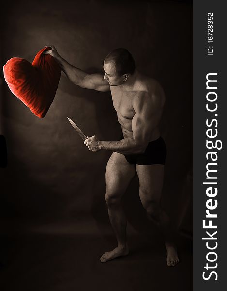 Muscular man with knife attacking red heart