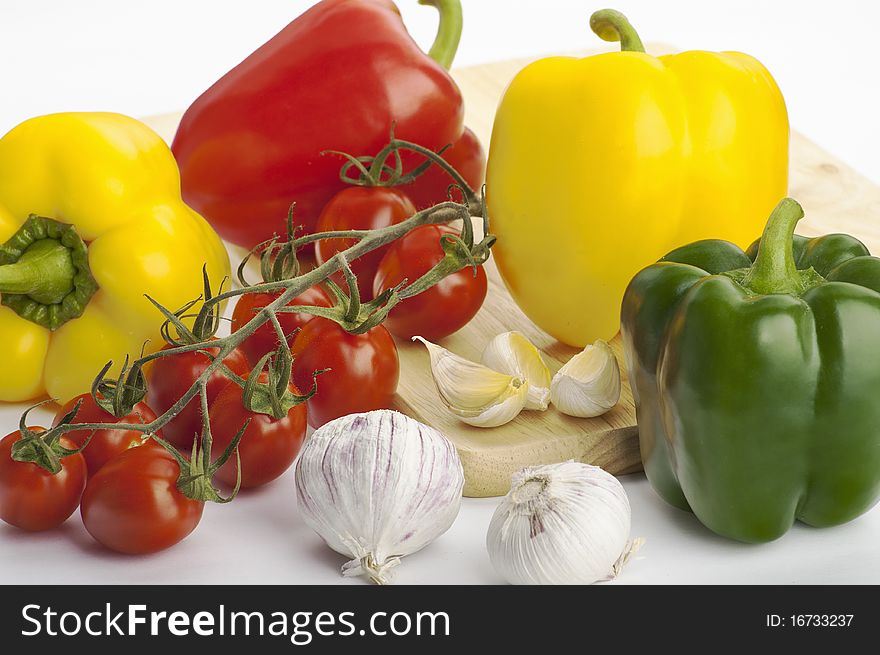 Green, yellow and red peppers, garlic and vine cherry tomatoes ready to cook on the white background. Green, yellow and red peppers, garlic and vine cherry tomatoes ready to cook on the white background