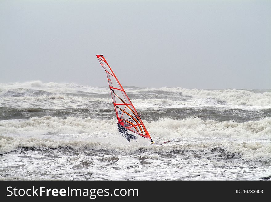 Surfer on windsurf with red sail on stormy sea with big wawes. Surfer on windsurf with red sail on stormy sea with big wawes