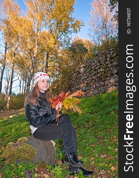 The girl in the autumn with a bouquet of leaves on a stone. The girl in the autumn with a bouquet of leaves on a stone