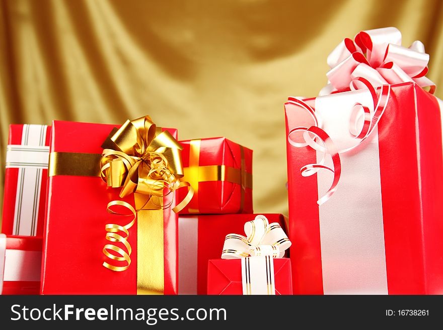 A lot of Christmas presents different values in the red packages with colorful bows on a gold background. A lot of Christmas presents different values in the red packages with colorful bows on a gold background