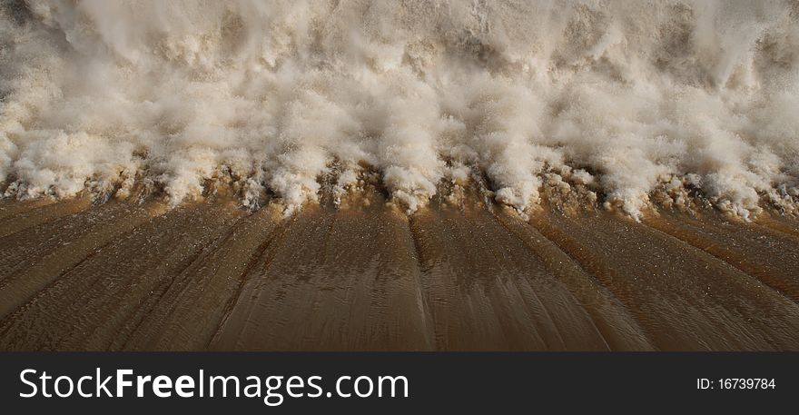 A birds eye view of brown water being released from a dam. A birds eye view of brown water being released from a dam