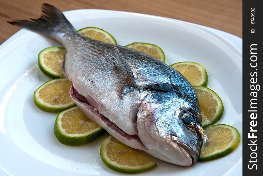 Fresh gilthead fish with slices of lemon on the plate, waiting to be cooked