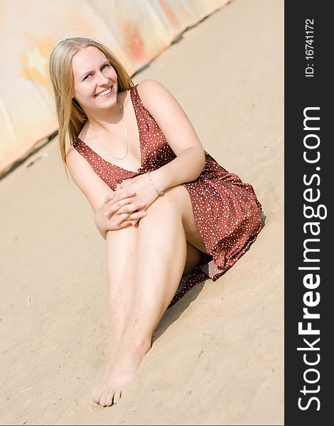 Summer portrait of the beautiful fair-haired girl who seat on the sand