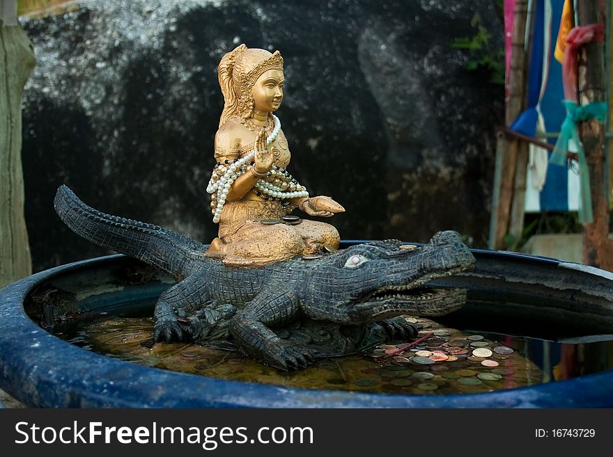 A figurine of an asian goddess sitting on a crocodile. A figurine of an asian goddess sitting on a crocodile.