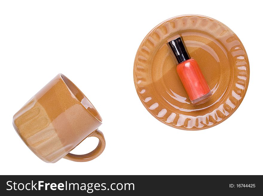 Orange nail polish laying on a brown plate next to a brown cup.