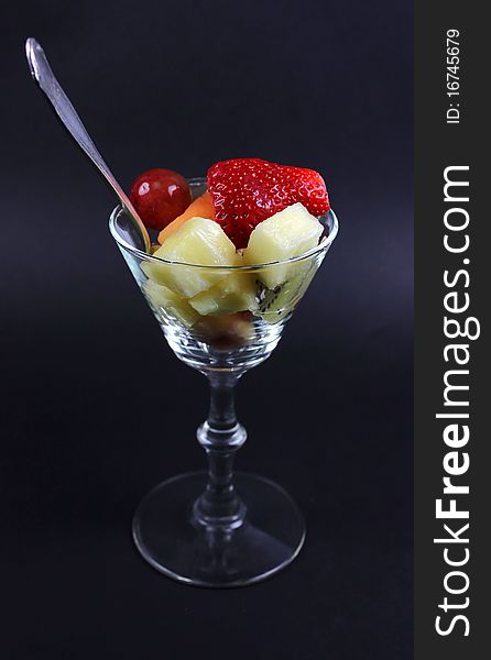 A cocktail glass with mised fruit and spoon isolated against black. A cocktail glass with mised fruit and spoon isolated against black