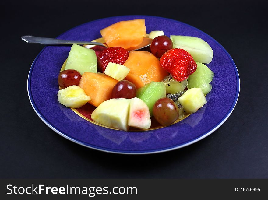 Mixed fruit and spoon on a colored plate isolated against black. Mixed fruit and spoon on a colored plate isolated against black.