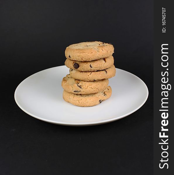 A stack of chocolate chip cookies on a white plate isolated against black. A stack of chocolate chip cookies on a white plate isolated against black.