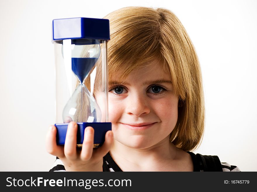 A vertical image of a young girl looking at the sand flowing in a hourglass. A vertical image of a young girl looking at the sand flowing in a hourglass