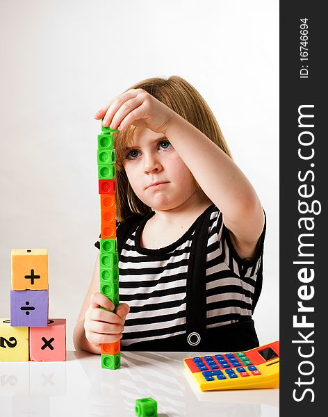 A vertical image of a young girl with counting blocks , building blocks and calculator.