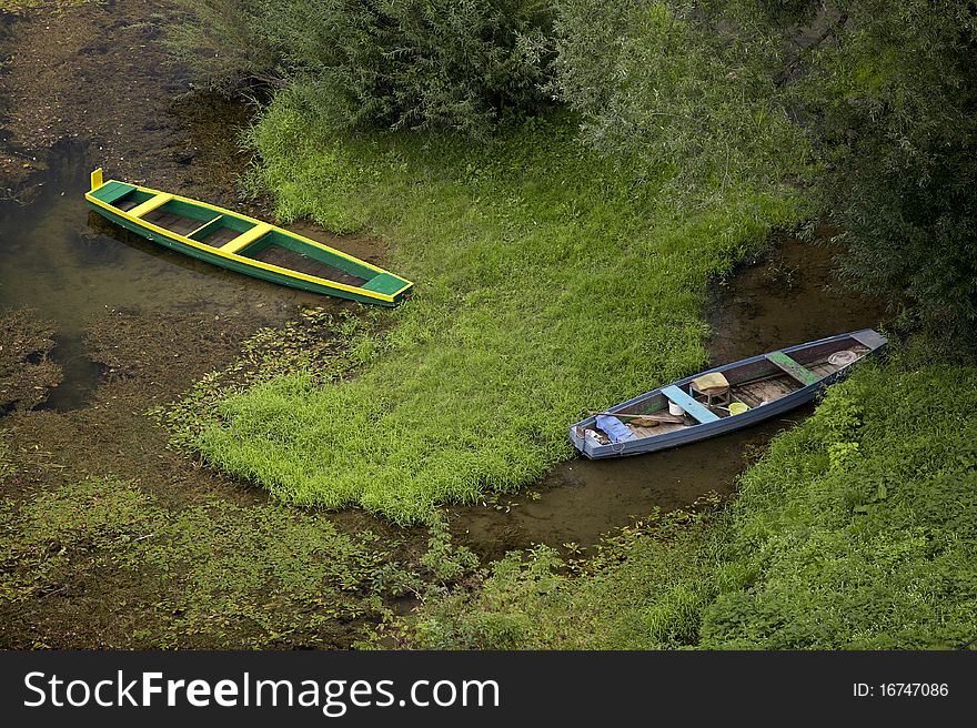 2 wooden river boats, shallow river, green grass and trees