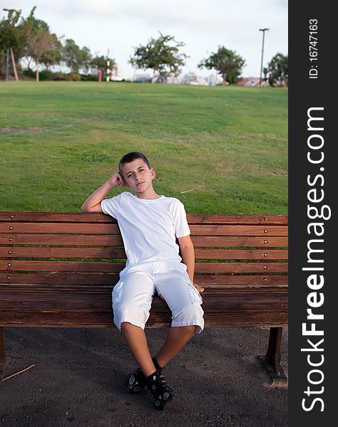 Boy sitting on a park bench with green meadow on the background . Boy sitting on a park bench with green meadow on the background .