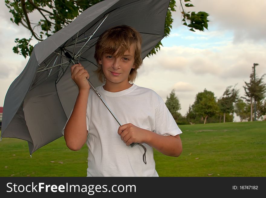 Boy looking at camera while under umbrella outside  . Boy looking at camera while under umbrella outside  .