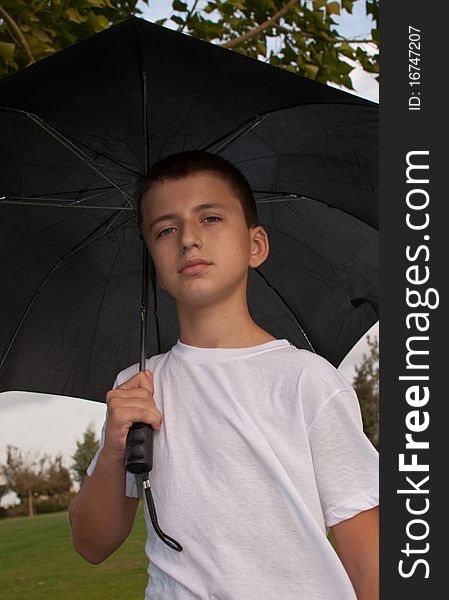 Boy looking at camera while under umbrella outside  . Boy looking at camera while under umbrella outside  .