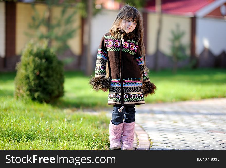 Adorable small girl with long dark hair in colorful warm clothes looks into the camera