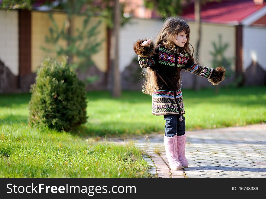 Adorable small girl with long dark hair in colorful warm clothes looks into the camera