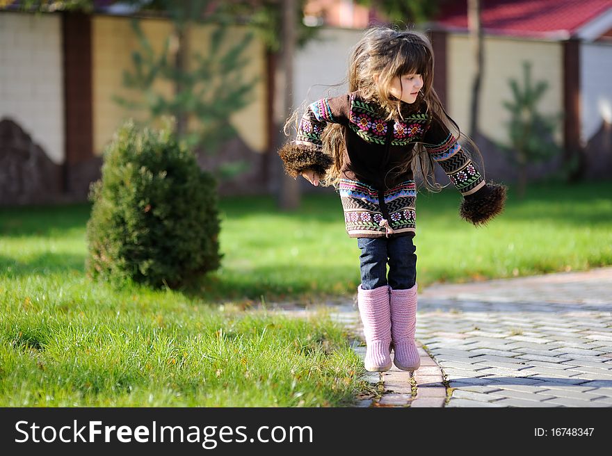 Adorable small girl with long dark hair in colorful warm clothes looks into the camera