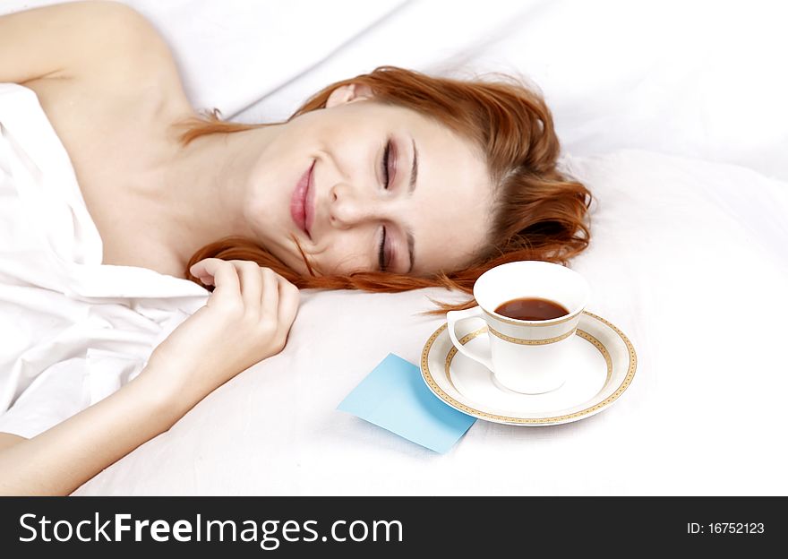 Pretty red-haired sleeping woman in white nightie lying in the bed near cup of coffee. Pretty red-haired sleeping woman in white nightie lying in the bed near cup of coffee.