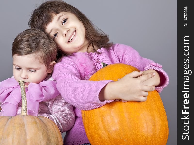 Two little sisters with pumpkin. Studio shot.