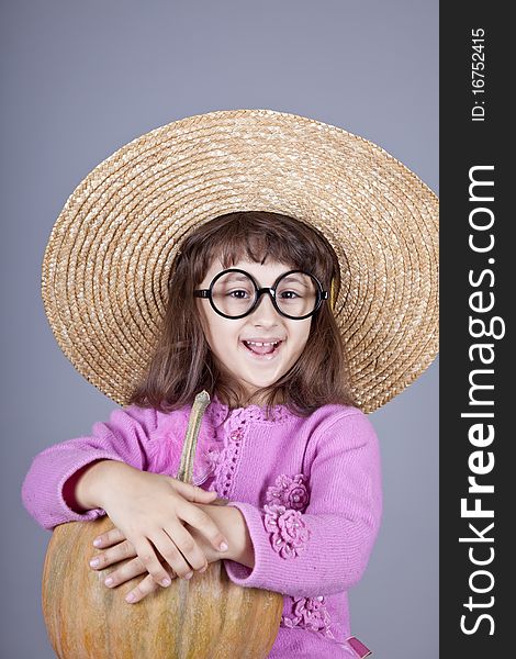 Funny girl in cap and glasses keeping pumpkin. Studio shot.