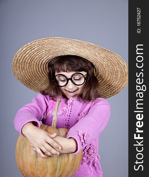 Funny girl in cap and glasses keeping pumpkin. Studio shot.