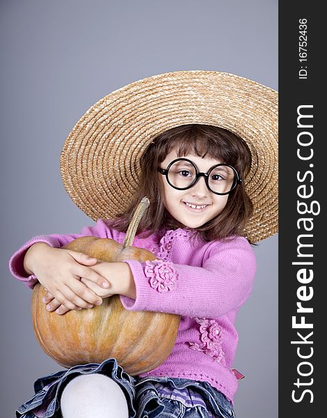 Funny girl in cap and glasses keeping pumpkin. Studio shot.