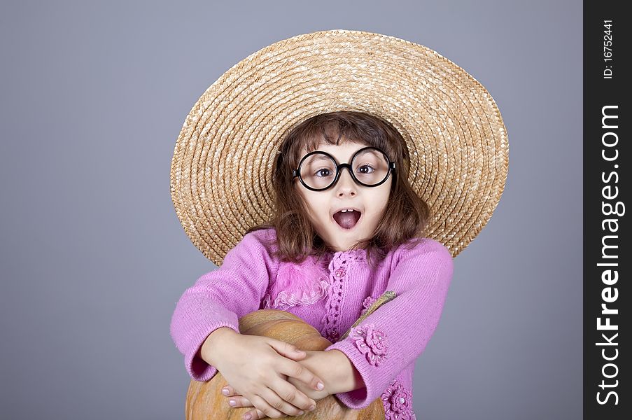 Funny girl in cap and glasses keeping pumpkin. Studio shot.