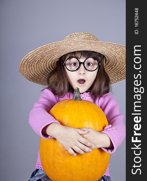 Funny girl in cap and glasses keeping pumpkin. Studio shot.