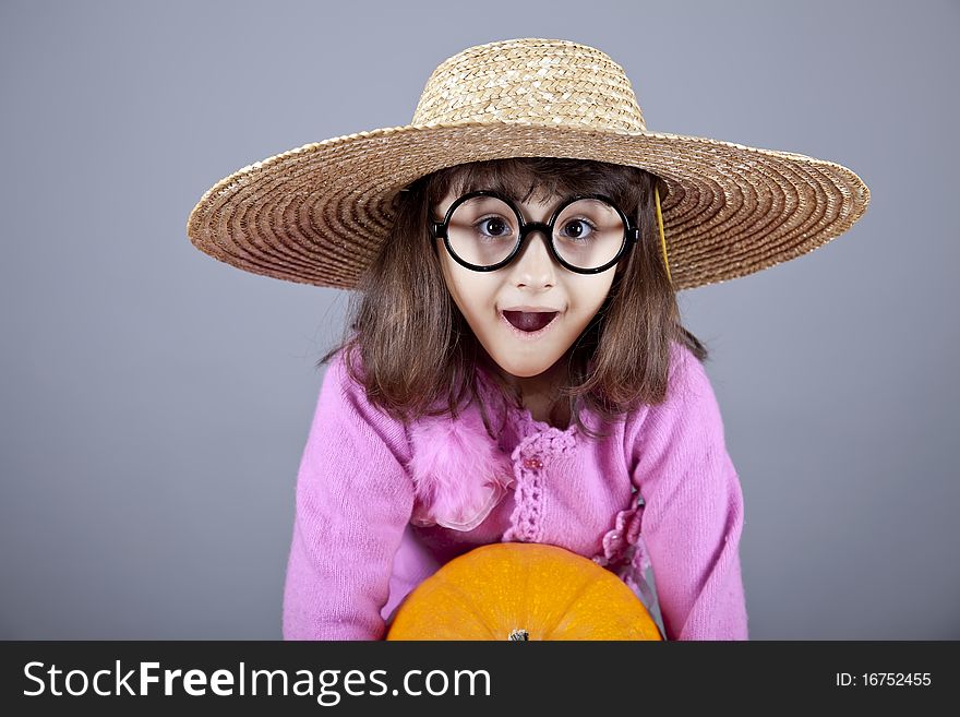 Funny girl in cap and glasses keeping pumpkin. Studio shot.