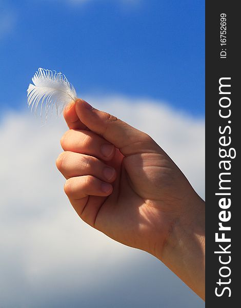 Hand holds a feather against blue sky