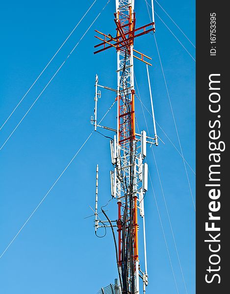 Tower of communications with antennas silhouetted against blue sky in town. Tower of communications with antennas silhouetted against blue sky in town.