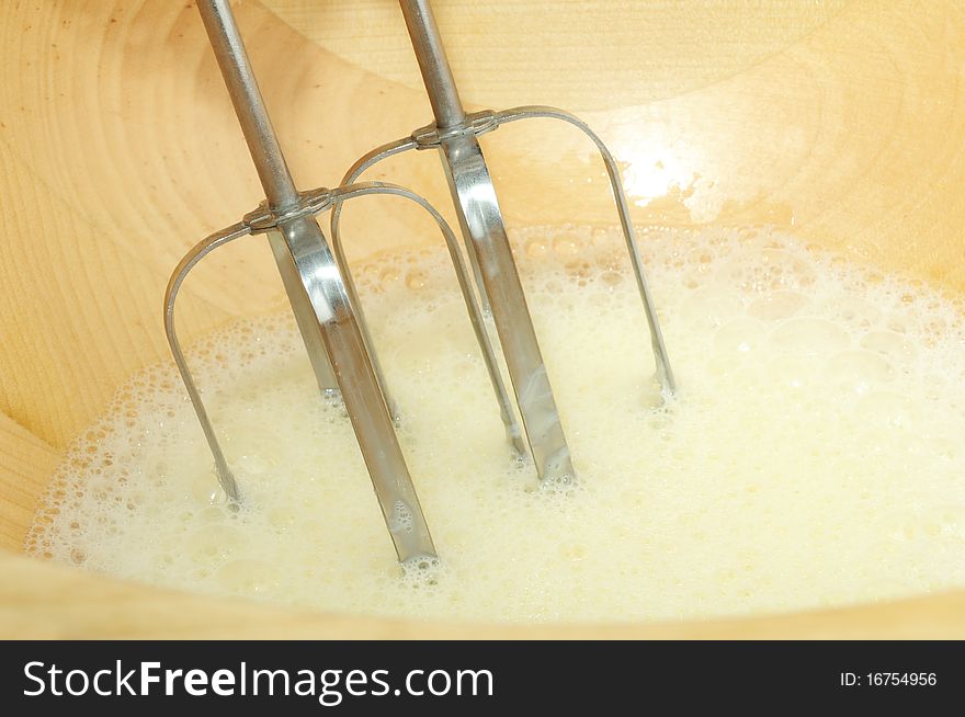 Beaten eggs with mixer whisks in a wooden bowl