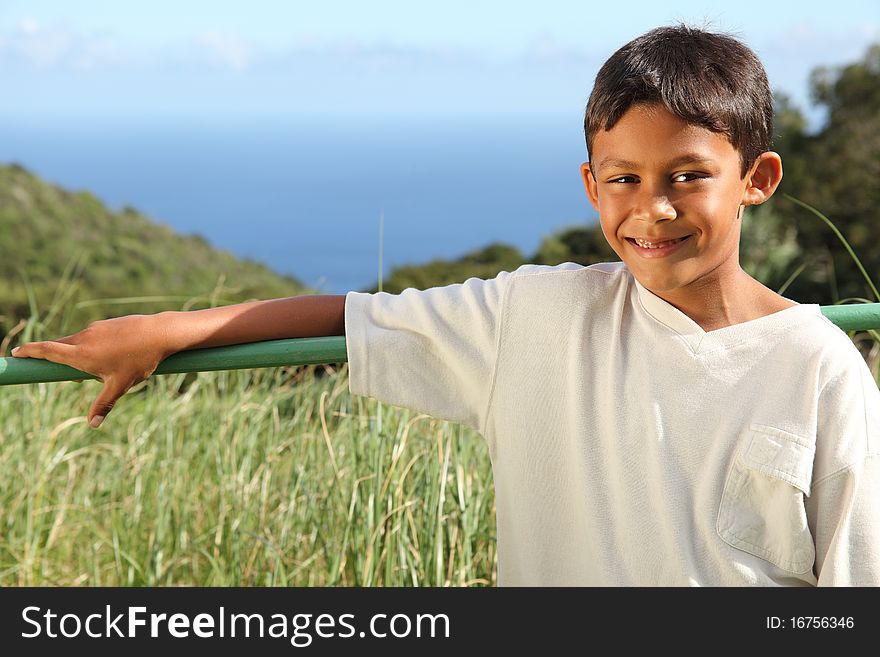 Young thnic boy, 10, standing against iron railing outdoors in the countryside sunshine with a cute smile. Young thnic boy, 10, standing against iron railing outdoors in the countryside sunshine with a cute smile