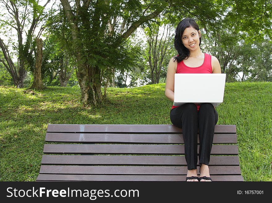 An Asian woman with a laptop sitting on a bench. An Asian woman with a laptop sitting on a bench