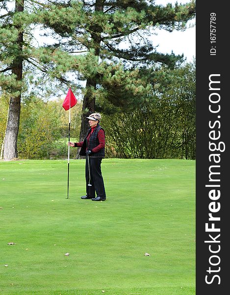 Female golfer standing on the green holding the putting flag. Female golfer standing on the green holding the putting flag