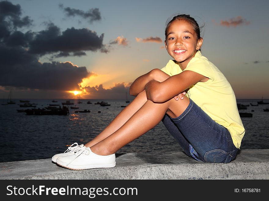 School girl with a big smile sitting by the sea at sunset. School girl with a big smile sitting by the sea at sunset