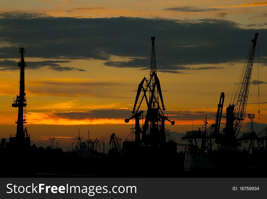 Silhouettes of cranes in the port against the dramatic red sky with dark clouds