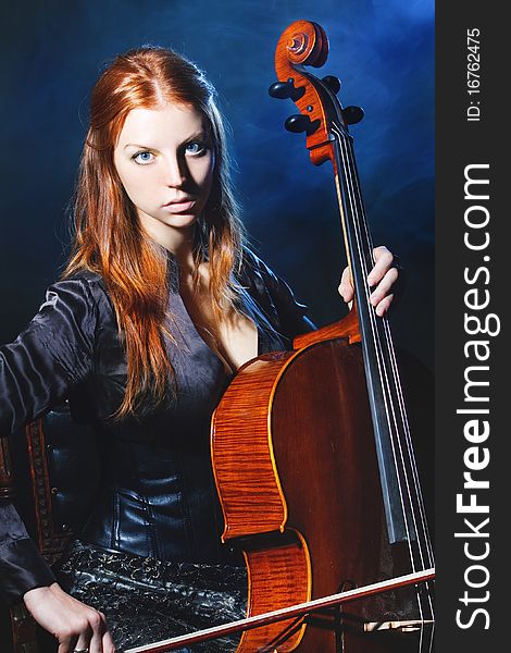 Young girl plays a violoncello against a dark blue smoke. Young girl plays a violoncello against a dark blue smoke