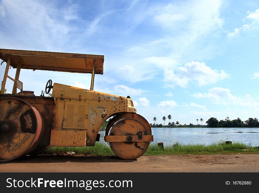 An old grungy road roller parked on the side of a lake