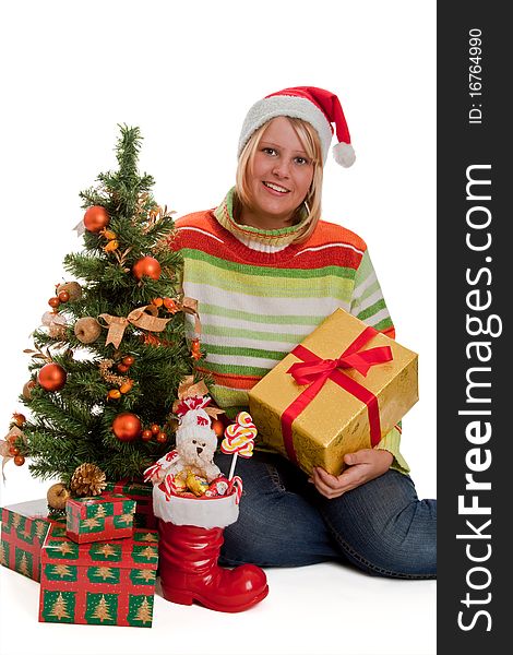 Young woman with santa hat sitting beside a christmas tree with christmas gifts - isolated. Young woman with santa hat sitting beside a christmas tree with christmas gifts - isolated