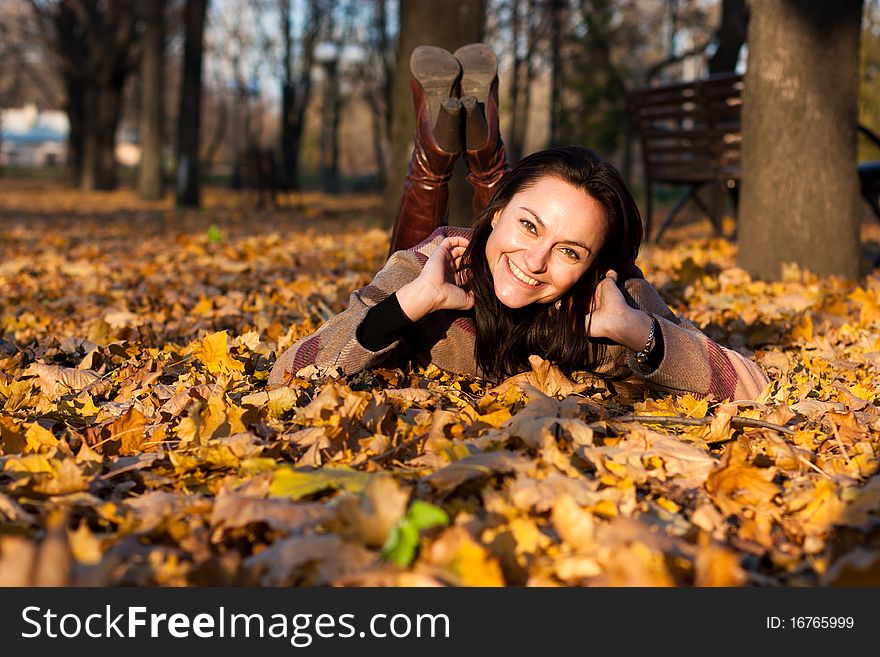 Beautiful young woman smiling lying down in autumn leaves in park. Beautiful young woman smiling lying down in autumn leaves in park
