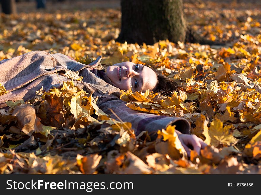Beautiful young woman lying in autumn leaves