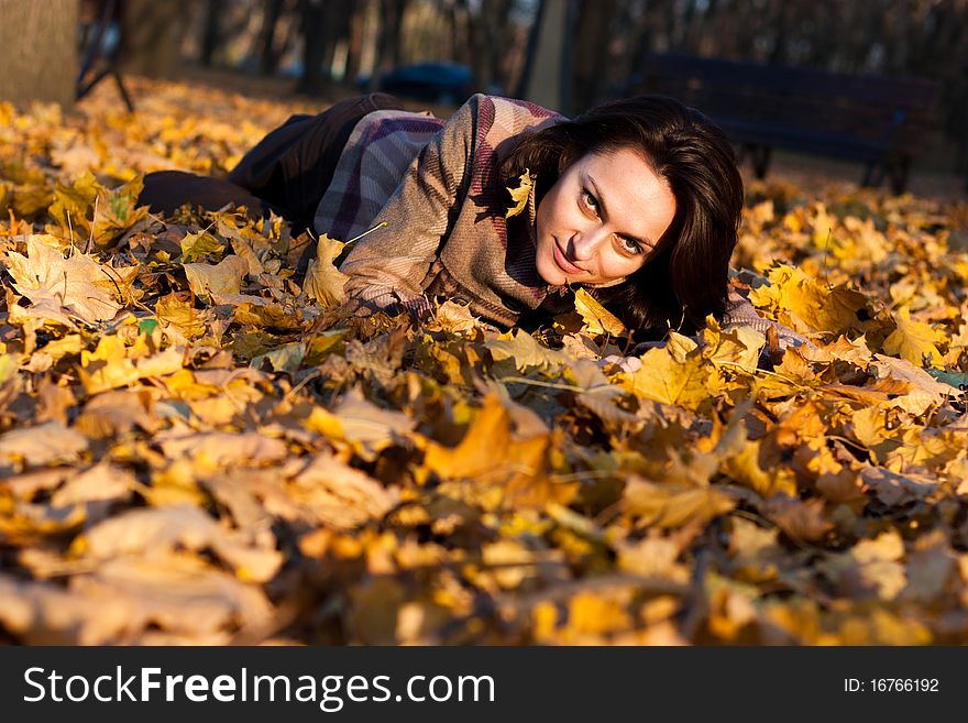 Beautiful young woman lying down in autumn leaves in park. Beautiful young woman lying down in autumn leaves in park